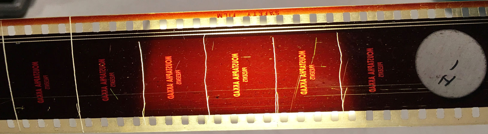 The head of a film with intentional damage. Frame lines are scratched into the emulsion, and the scratches extend into the soundtrack. A sticker in the picture area identifies the reel.
